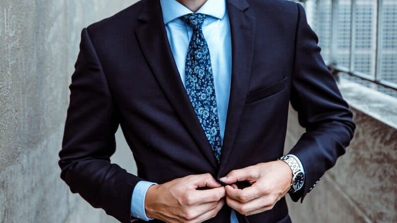 man wearing black and teal dress suit standing near gray wall
